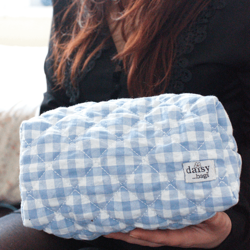 A young women holding the Nina blue makeup bag