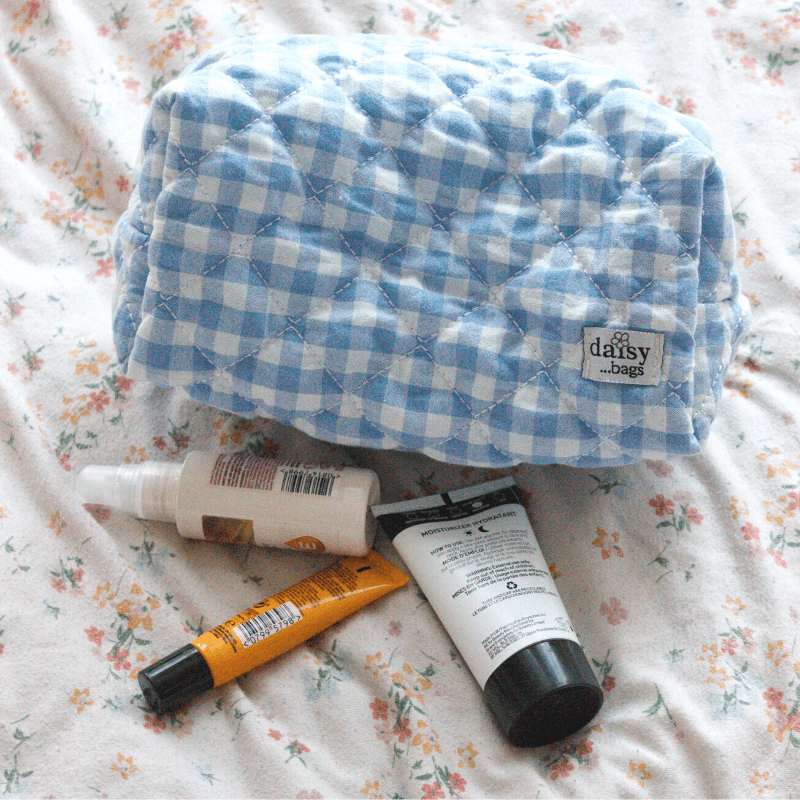 The Nina blue makeup bag on a floral bed sheet with 3 skincare products