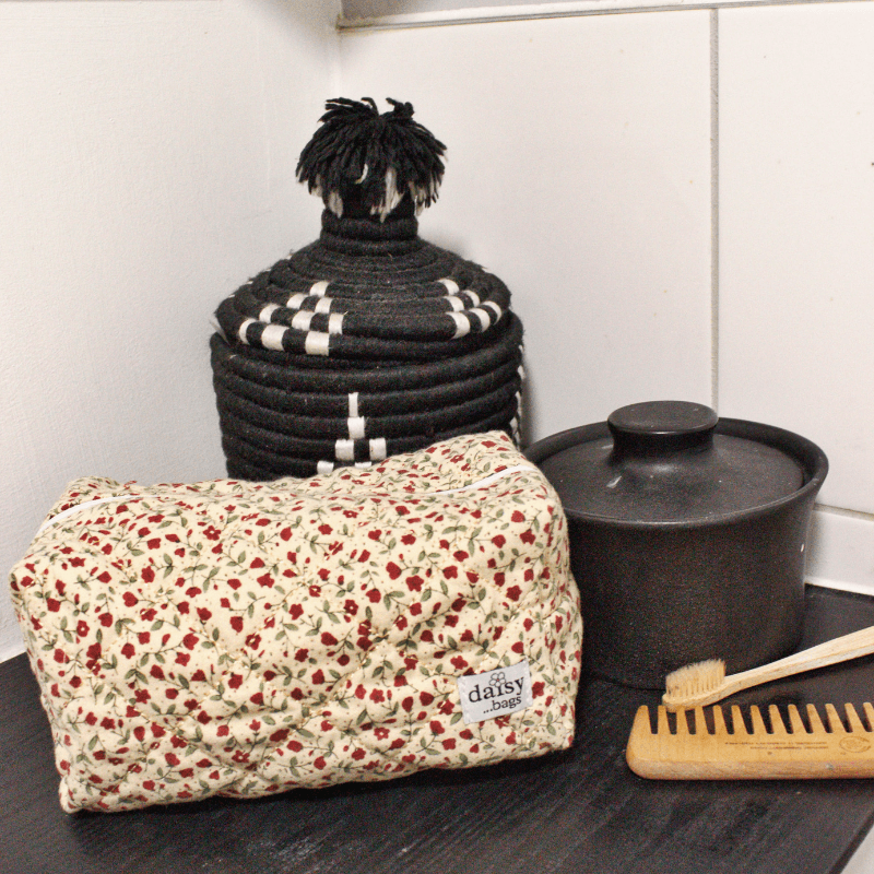 The Rose floral makeup bag on a bathroom counter with black ornaments in the background