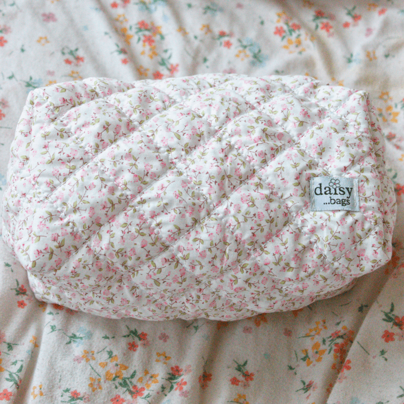 The Daisy floral makeup bag on a floral bed sheet