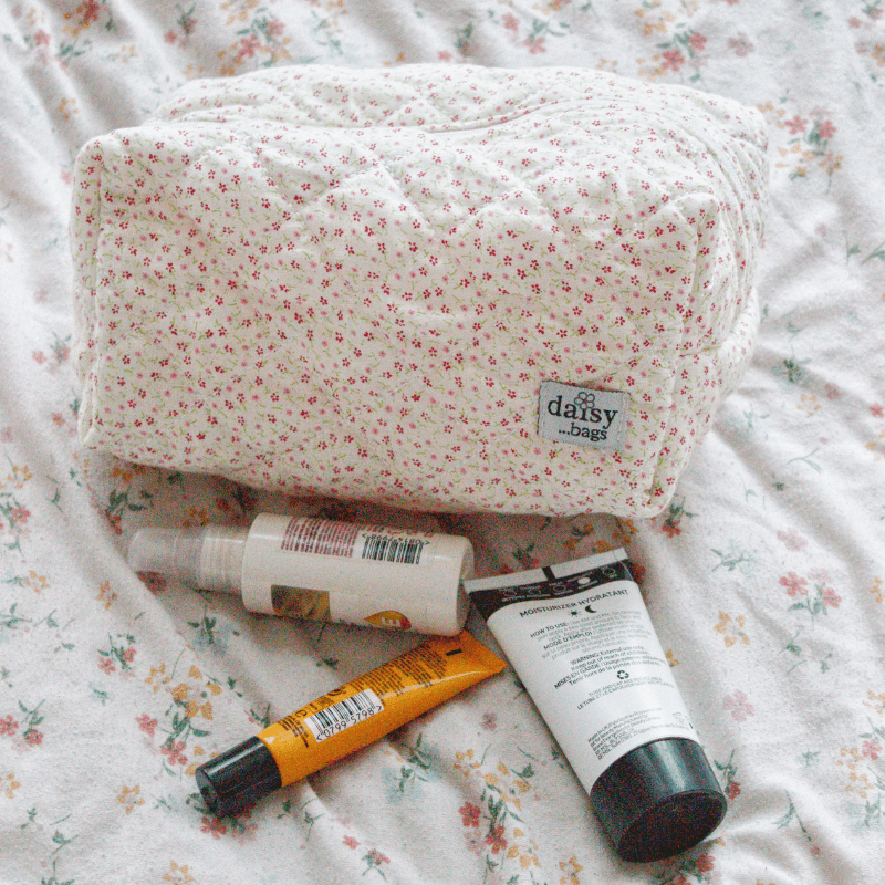 The Bloom floral makeup bag on a floral bed sheet with 3 skincare products